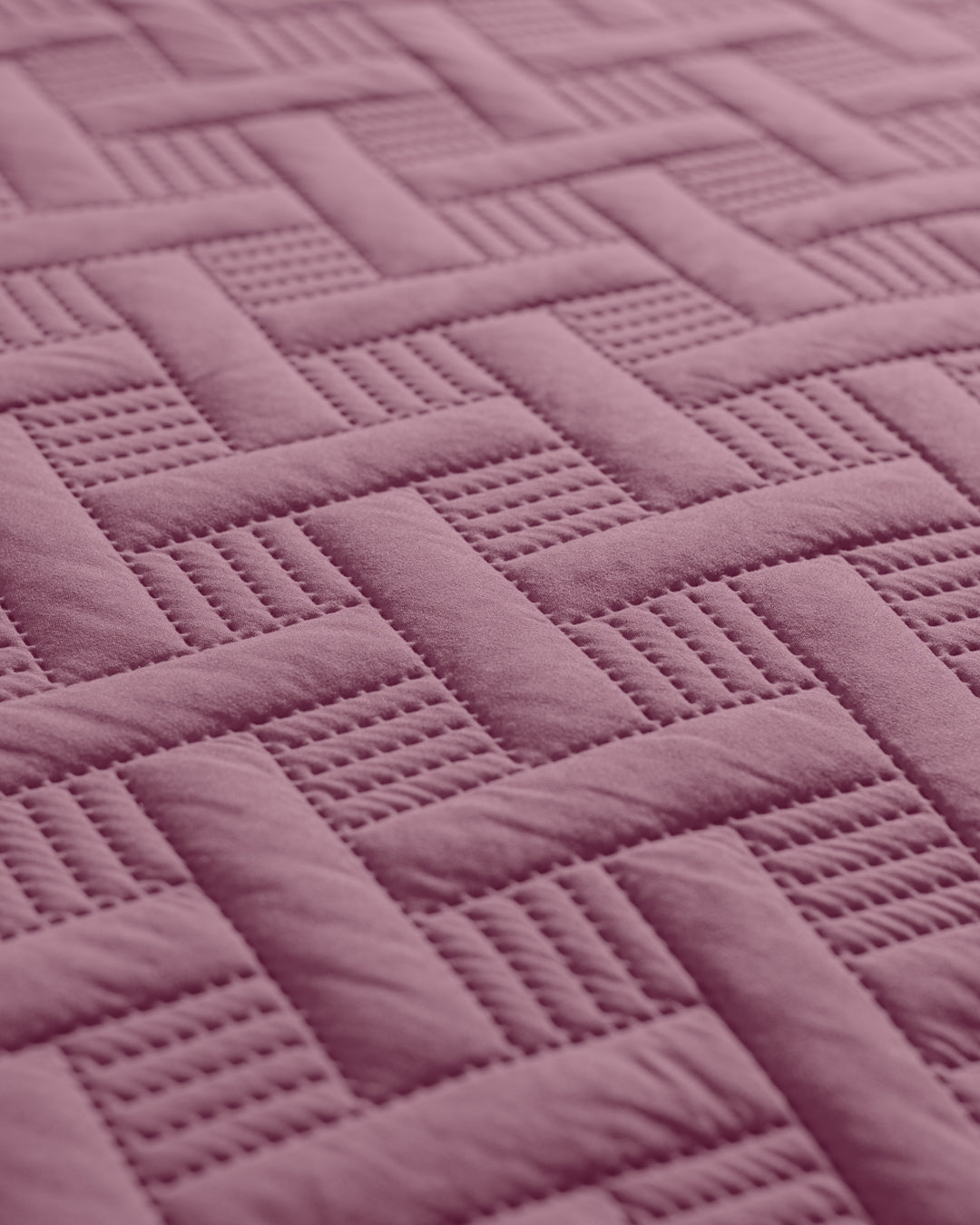 Close-up of the Juego de Edredón Ligero Espíritu by Intima Hogar, showcasing its quilted pinkish-purple fabric with an interwoven basketweave pattern, alternating between smooth and textured sections.