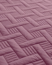 Close-up of the Juego de Edredón Ligero Espíritu by Intima Hogar, showcasing its quilted pinkish-purple fabric with an interwoven basketweave pattern, alternating between smooth and textured sections.