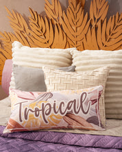 A stylish dormitorio features the Edredón Ligero Provenza by Intima Hogar, paired with cream and white textured pillows, a “Tropical” long pillow, and a unique wooden headboard shaped like palm leaves.