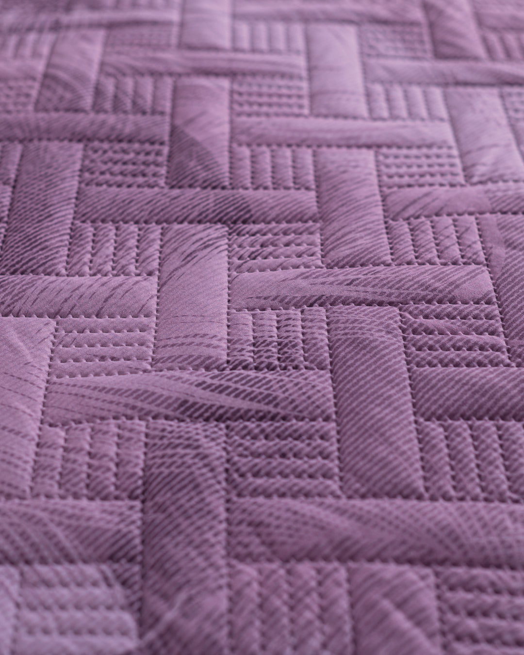 Close-up of the Edredón Ligero Provenza by Intima Hogar, featuring purple quilted fabric with a geometric pattern inspired by paisajes de Provenza—perfect for adding a textured, three-dimensional effect to your dormitorio.