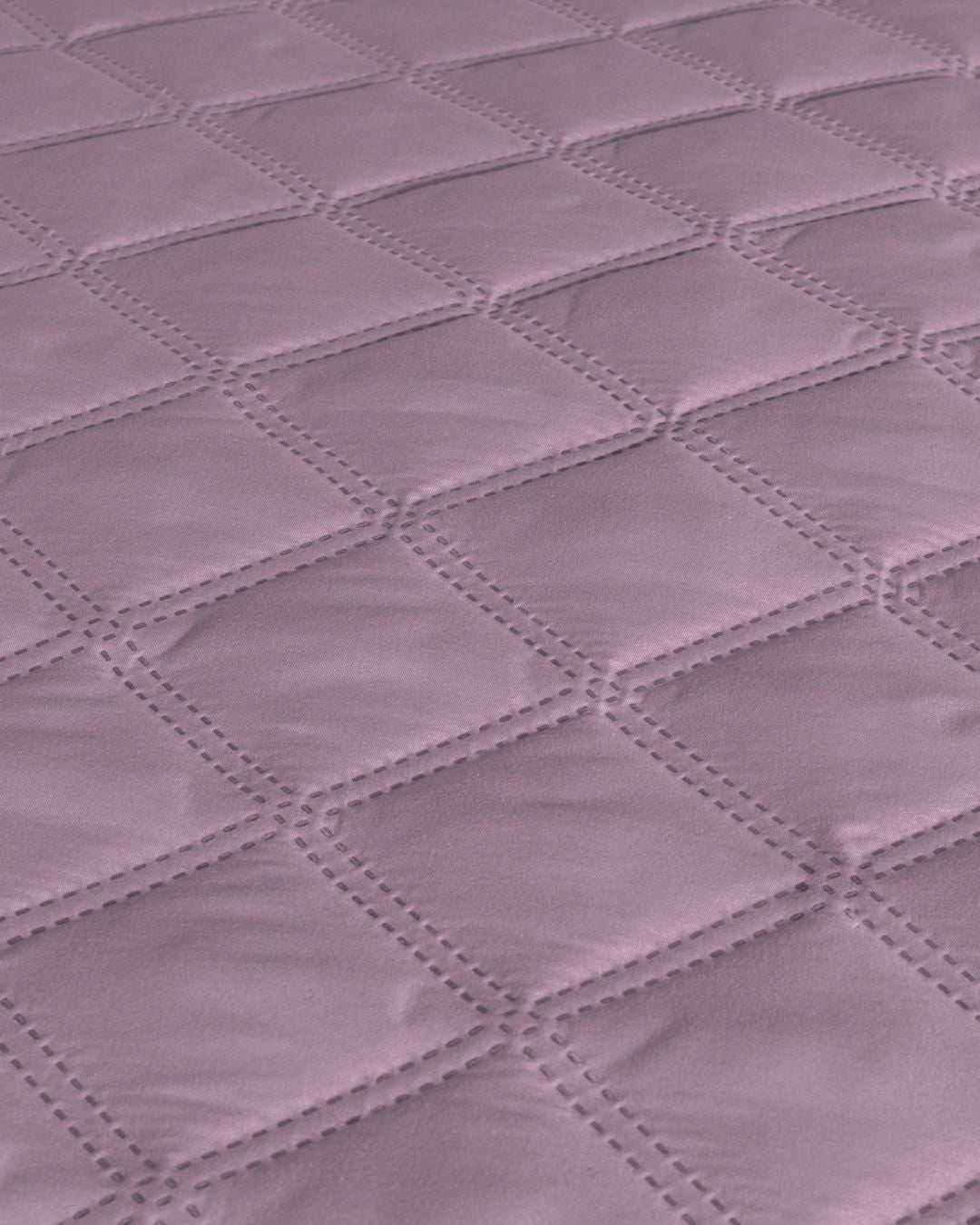 Close-up of the Juego de Edredón Ligero Lima by Intima Hogar, showing a soft mauve quilted fabric with a diamond-stitched pattern and smooth, padded texture.