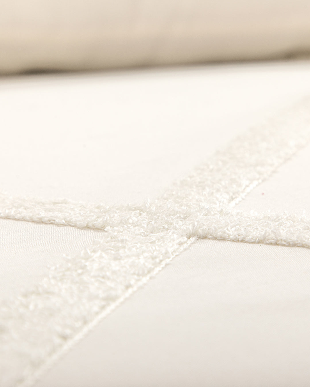 Close-up of Intima Hogar’s Juego de Duvet Luxury Arena, featuring cream-colored fabric with intersecting textured, fuzzy lines forming a cross pattern on a smooth background.