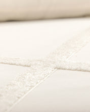 Close-up of Intima Hogar’s Juego de Duvet Luxury Arena, featuring cream-colored fabric with intersecting textured, fuzzy lines forming a cross pattern on a smooth background.