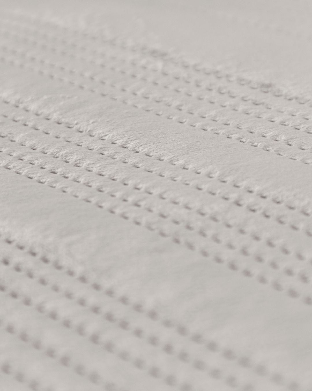 Close-up of the Juego de Edredón Velvet Silencio by Intima Hogar, featuring a white textured surface with small, evenly spaced raised dots in parallel lines for a subtle, elegant pattern.