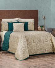 A neatly made bed features the Intima Hogar Juego de Edredón Velvet Vida, a beige leaf-patterned reversible set with teal accents and matching fundas decorativas. A brown headboard and modern nightstand decor complete the stylish look.