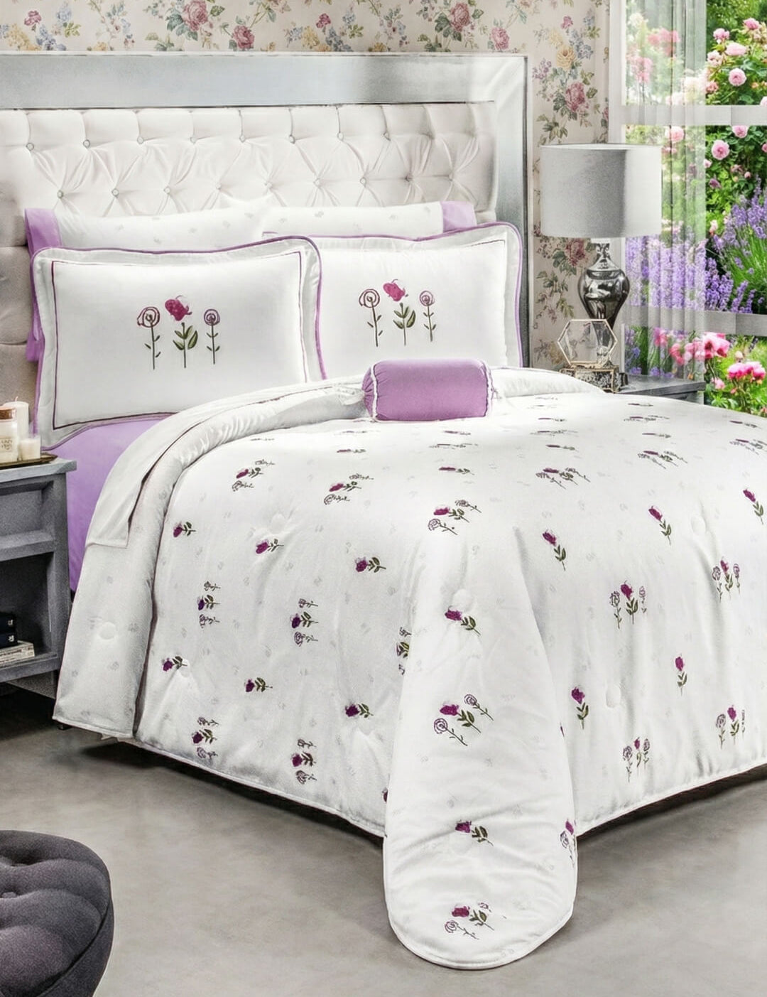 A neatly made bed features the Coordinado de Edredón Ultra Suave Amore by Intima Hogar, with white bedding and purple floral designs, matching pillows, a lavender throw pillow, floral wallpaper, tufted headboard, and a window with greenery.