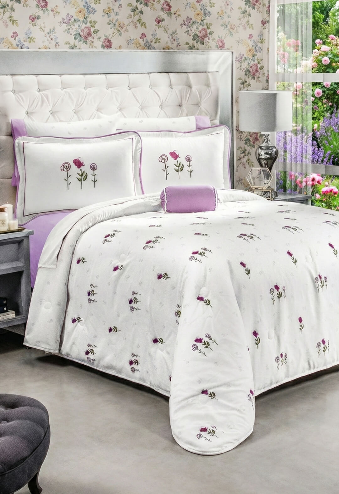 A neatly made bed features the Coordinado de Edredón Ultra Suave Amore by Intima Hogar, with white bedding and purple floral designs, matching pillows, a lavender throw pillow, floral wallpaper, tufted headboard, and a window with greenery.