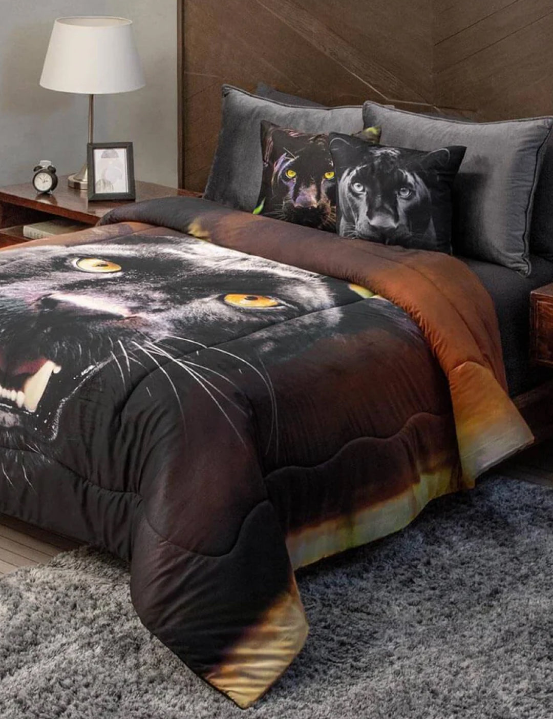 A modern bedroom features a bed dressed with bedding and the Cojín Estampado Black Panther by Intima Hogar, creating a bold look. The bed stands against a wood headboard beside a nightstand with lamp and clock, while a gray rug covers the floor.