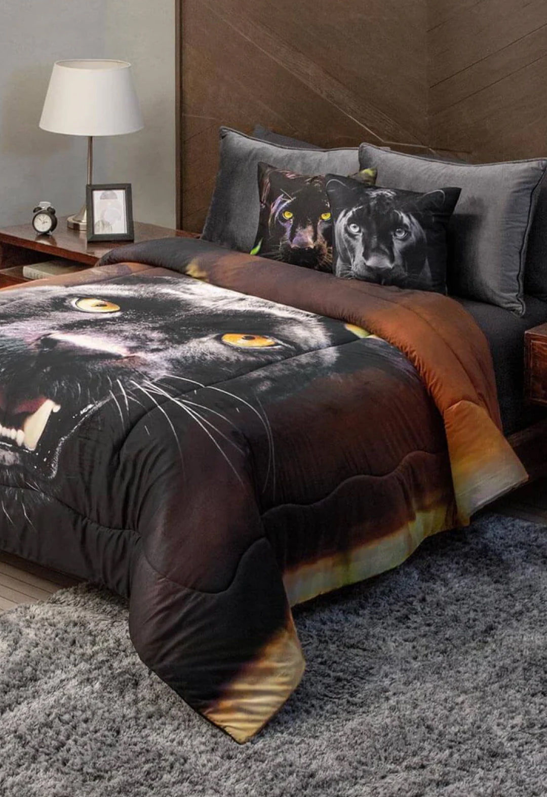 A modern bedroom features a bed dressed with bedding and the Cojín Estampado Black Panther by Intima Hogar, creating a bold look. The bed stands against a wood headboard beside a nightstand with lamp and clock, while a gray rug covers the floor.