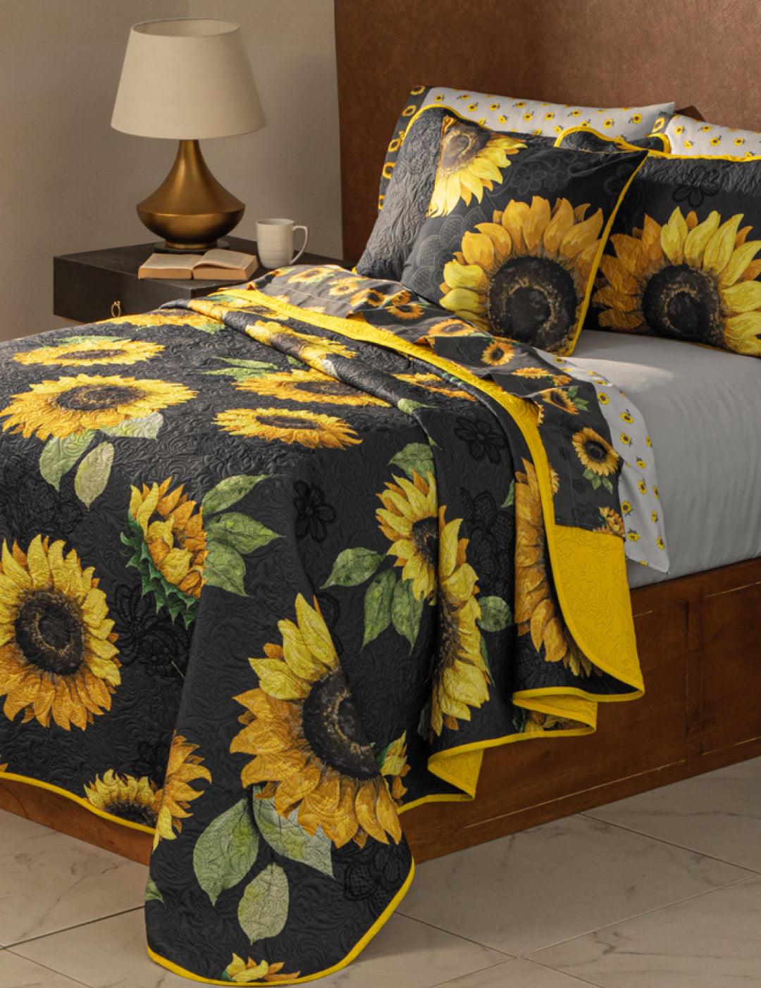 A neatly made bed with the Coordinado de Edredón Ultra Suave Amarelo by Intima Hogar, featuring bright yellow sunflowers and green leaves, sits beside a wooden nightstand with a lamp, books, and a cup—perfect for your room.