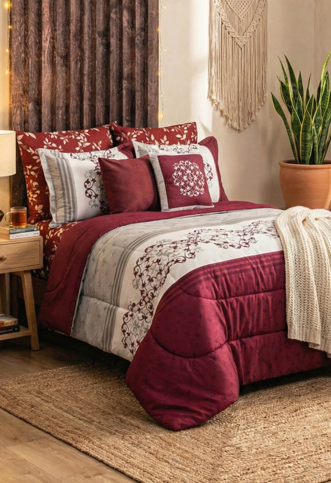 A cozy bedroom with the Intima Hogar Juego de Edredón Super Suave Eliza in red and white floral, decorative pillows, a knitted blanket, a bedside table with lamp, a houseplant in terracotta pot, and a woven wall hanging above the bed.