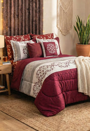 A cozy bedroom with the Intima Hogar Juego de Edredón Super Suave Eliza in red and white floral, decorative pillows, a knitted blanket, a bedside table with lamp, a houseplant in terracotta pot, and a woven wall hanging above the bed.