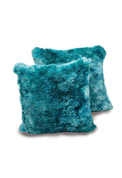 Two square Juego De Cojín Everest by Intima Hogar in teal with a soft, shaggy texture are stacked slightly overlapping on a plain white background, bringing style and comfort to any space.