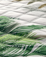 Close-up of the Juego de Edredón Tropical by Intima USA, showcasing a green and white palm leaf print on ultra-soft fabric. The padded comforter features visible diamond stitching for an elegant tropical look.