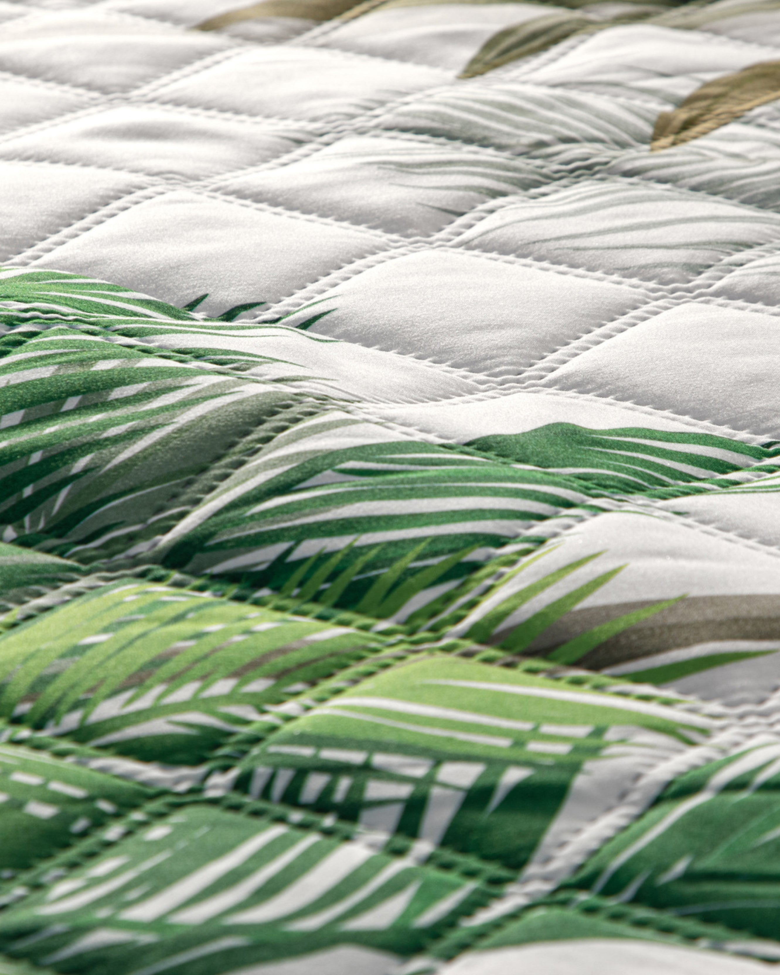 Close-up of the Juego de Edredón Tropical by Intima USA, showcasing a green and white palm leaf print on ultra-soft fabric. The padded comforter features visible diamond stitching for an elegant tropical look.