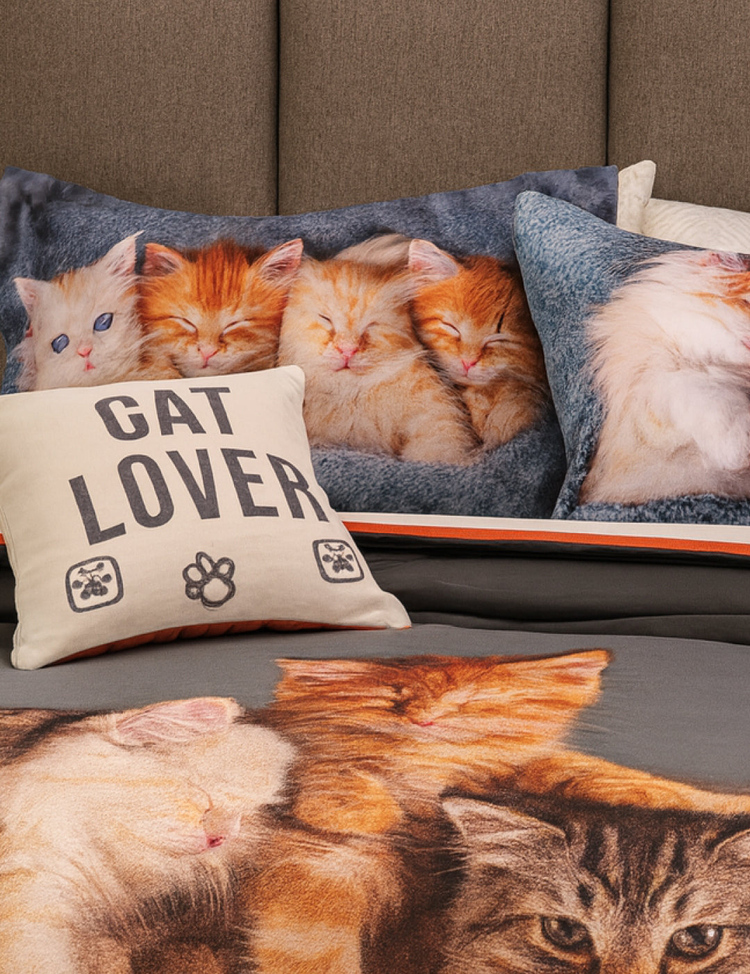 The Intima Hogar Coordinado de Edredón Cat Lover incluye un edredón gris-blanco con cojines decorativos: uno dice "Cat Lover" con huellas, y otros muestran fotos de gatitos dormidos y acurrucados sobre cubrecamas delgados.