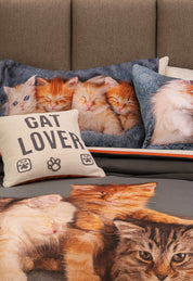 The Intima Hogar Coordinado de Edredón Cat Lover incluye un edredón gris-blanco con cojines decorativos: uno dice "Cat Lover" con huellas, y otros muestran fotos de gatitos dormidos y acurrucados sobre cubrecamas delgados.