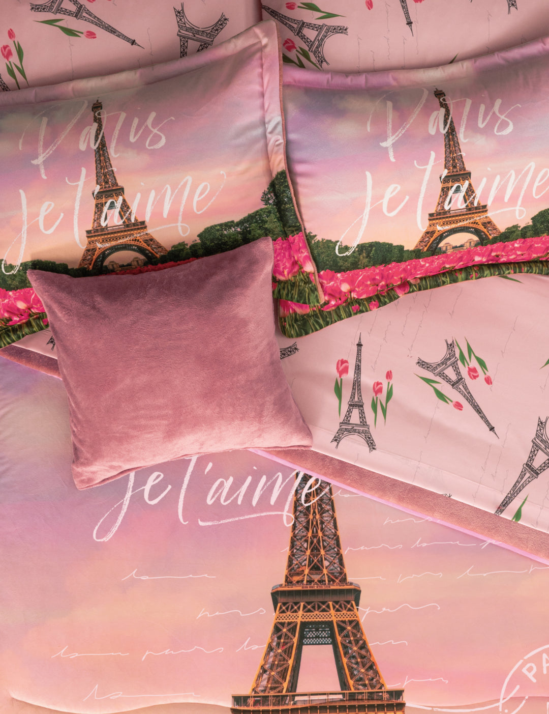 A close-up of the Coordinado de Cobertor Supremo Romantique by Intima Hogar, a pink floral bedspread set with Eiffel Tower, tulip designs, and “Paris Je t’aime”, topped with a soft mauve throw pillow.