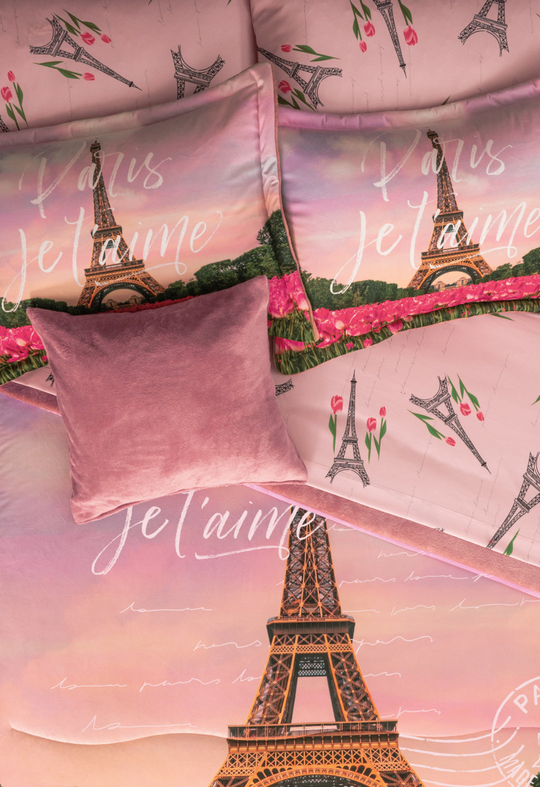 A close-up of the Coordinado de Cobertor Supremo Romantique by Intima Hogar, a pink floral bedspread set with Eiffel Tower, tulip designs, and “Paris Je t’aime”, topped with a soft mauve throw pillow.