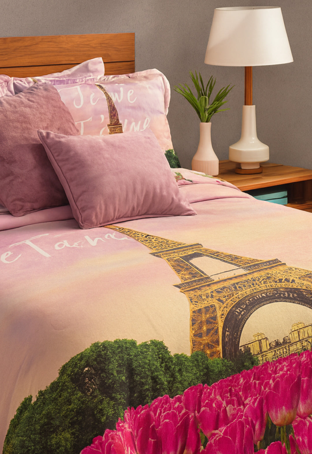 The Coordinado de Cobertor Supremo Romantique by Intima Hogar features pink and lavender microfiber with Eiffel Tower, tulips, and "Je t’aime" designs. A lamp, plant, and wooden nightstand complete this charming bedroom set.