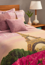 The Coordinado de Cobertor Supremo Romantique by Intima Hogar features pink and lavender microfiber with Eiffel Tower, tulips, and "Je t’aime" designs. A lamp, plant, and wooden nightstand complete this charming bedroom set.